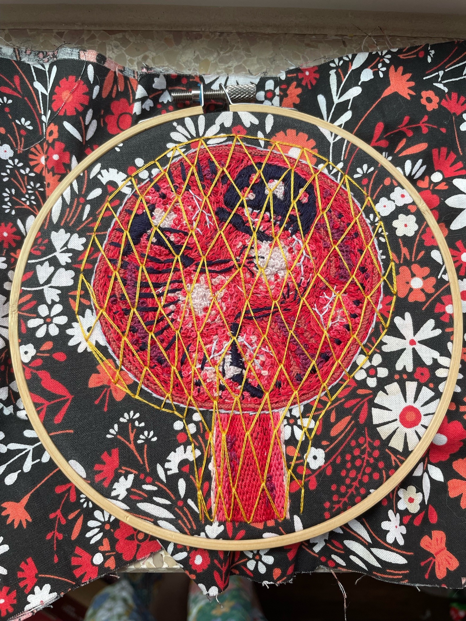 Embroidery piece of Ruidus, the red moon of Exandria from campaign three of Critical Role. Predathos is depicted as a dark navy skeleton of a reptile curled inside the moon. The entire moon is surrounded by a golden net reminiscent of the Divine Gate, and a beam of red light extends from Ruidus containing several figures traveling between Exandria and the moon.